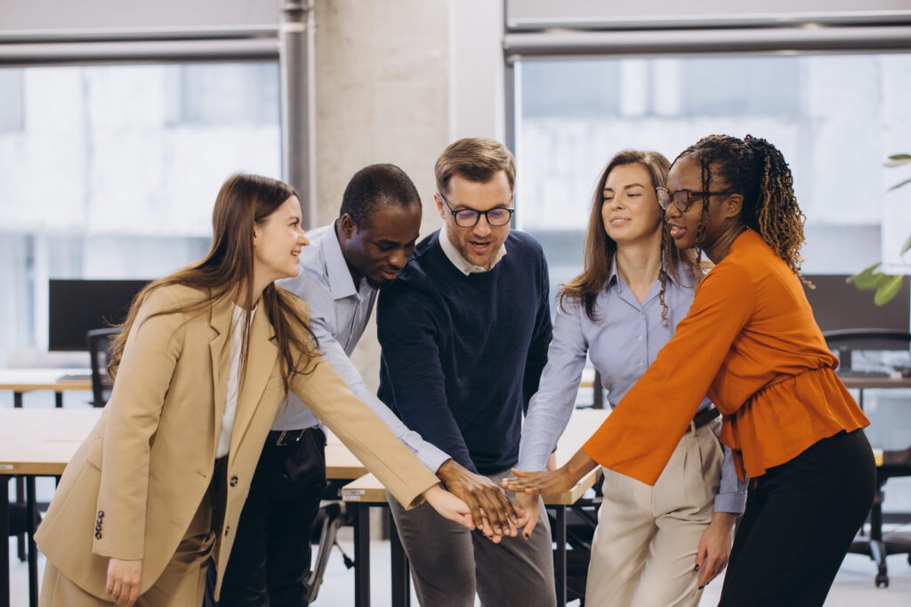Diverse businesspeople joining hands in office, symbolizing teamwork, collaboration, and unity in achieving shared goals